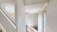 Located at 1800 FM 1092 Rd in Missouri City, TX, this two-story residence offers a thoughtfully laid-out floor plan distributed across two levels. The ground floor serves as the main living and kitchen area, featuring durable wood-look vinyl plank flooring throughout. The kitchen is well-equipped with stainless steel appliances, including a range and dishwasher, complemented by white cabinetry, dark granite-style countertops, and a mosaic tile backsplash — creating a clean, modern aesthetic. The open living area is highlighted by a ceiling fan with light fixture, crown molding, and a sliding glass door that allows natural light to pour in. A carpeted staircase connects the two floors, leading to the upper level where the spacious primary bedroom is located. The bedroom is generously sized, finished with plush carpet, a ceiling fan, and a textured ceiling. It includes a walk-in closet with built-in shelving, providing ample storage. A wall of windows allows natural light to brighten the room. Throughout the space, neutral gray tones, white trim, and textured ceilings contribute to a bright, cohesive, and move-in-ready atmosphere.