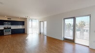 Located on Hollywood Boulevard in Los Angeles, this modern single-floor residence offers a clean, contemporary design throughout. The open-concept living and dining area is expansive and light-filled, featuring warm wood-tone flooring and large floor-to-ceiling windows with sliding glass doors that invite abundant natural light and offer views of the surrounding palm-tree-lined neighborhood. The kitchen is appointed with dark navy cabinetry, white countertops, a tile backsplash, and a full suite of stainless steel appliances including a refrigerator, range, microwave, and dishwasher. The bedroom is generously proportioned, finished with plush carpeting and a large window that continues the theme of natural light. Two bathrooms are present, each featuring a full soaking tub with shower, clean white surrounds, wood-tone flooring, and dark vanity cabinetry with white countertops. Additional hallway and utility spaces connect the rooms seamlessly, with consistent wood-tone flooring throughout the non-carpeted areas. The overall aesthetic is modern and minimalist, with crisp white walls, recessed lighting, and thoughtful finishes that create a bright, functional, and cohesive living environment.
