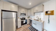 This efficiently designed one-bedroom, one-bathroom unit offers a thoughtful open-concept floor plan that maximizes every square foot. Light-toned wood flooring flows throughout the main living areas, lending warmth and continuity to the space.

The kitchen is a standout feature, outfitted with soft gray shaker-style cabinetry, white subway tile backsplash, light countertops, and a full suite of stainless steel appliances including a refrigerator, range, microwave, and dishwasher. A double-basin sink completes this functional and stylish space.

The open living area connects seamlessly to the kitchen and extends toward a glass-panel door that opens to a private balcony, offering views of the surrounding cityscape and hills. Recessed lighting and a textured ceiling add to the welcoming ambiance.

The bedroom is a comfortable, well-lit retreat featuring plush carpet, a large window framing scenic outdoor views, and clean white walls. A closet provides convenient storage.

The bathroom features a white vanity with an undermount sink, a soaking tub and shower combination with a window for natural light, and hardwood-style flooring. A hallway connects all rooms, completing the efficient and cohesive layout of this modern unit.