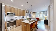 This thoughtfully designed one-bedroom, one-bathroom residence spans two floors, offering a generous and well-appointed layout with contemporary finishes throughout. The main floor features an open-concept kitchen and living area, where warm wood cabinetry, white quartz countertops, a full suite of stainless steel appliances, and a central island with seating create an inviting and functional space. Stylish pendant lighting anchors the kitchen, which flows seamlessly into the living room. Large floor-to-ceiling windows and a private balcony off the living area flood the space with natural light and provide views of the landscaped courtyard and pool below. Light hardwood flooring runs throughout the main level, enhancing the bright and airy ambiance. The upper floor hosts the bedroom, a carpeted and comfortable retreat with a large window offering exterior views, ample closet space, and a neutral palette. The full bathroom features a wood-toned vanity with a backlit mirror, white quartz countertop, and a glass-enclosed shower with subway tile surround. The overall design blends modern aesthetics with warm materials, creating a cohesive and inviting living environment across both levels.
