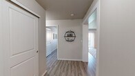 Located in the Harbour Landing community of Regina, Saskatchewan, this 2-bedroom, 1-bathroom unit offers a thoughtfully designed single-floor layout. The open-concept kitchen and living area serves as the heart of the space, featuring dark-stained cabinetry, light countertops with a breakfast bar accommodating two bar stools, black appliances including a refrigerator and range, and a subway tile backsplash. The kitchen flows seamlessly into the living room, which is bathed in natural light from a large sliding glass door fitted with vertical blinds. Light-toned laminate flooring extends throughout the unit, complementing the neutral grey and white wall palette.

The welcoming hallway, accented by decorative wall shelving, connects the living areas to the two bedrooms. Both bedrooms are cozy and functional, each featuring a window for natural light and overhead ventilation. The primary bedroom offers a quiet retreat with room for a full-sized bed and nightstands. The full bathroom includes a clean white tub-shower combination. The overall ambiance is modern and bright, with a consistent, contemporary aesthetic carried throughout every room.