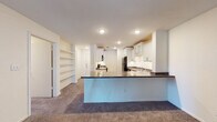Located at 5016 Oakbrook Dr in Lansing, Michigan, this single-floor residence offers a well-organized and functional layout throughout. The kitchen is a standout feature, showcasing crisp white shaker-style cabinetry — including glass-front upper cabinets — paired with rich dark stone-look countertops. Black appliances, including a refrigerator, electric range, over-the-range microwave, and dishwasher, complement the clean aesthetic. Light wood-look flooring runs through the kitchen, adding warmth and easy maintenance. A peninsula counter extends the workspace and provides a natural division between the kitchen and adjacent living area. The living space features plush carpeting and benefits from natural light through windows and a glass-panel exterior door that offers views to the outdoors. Built-in open shelving in the living area provides convenient storage and display space. The bedrooms are carpeted and well-proportioned, each equipped with sliding mirrored closet doors and windows that invite natural light; one bedroom also features a ceiling fan. The bathroom includes a double-sink vanity with white cabinetry, dark countertops, and wood-look flooring, offering a practical and polished finish throughout.