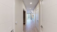 Located in Pompano Beach, Florida, this studio at Mayla 710 presents a thoughtfully designed single-floor layout with a clean, modern aesthetic throughout. Light-toned, wood-look tile flooring runs continuously across the entire space, lending a cohesive and airy feel from entry to living area.

A long, well-lit entry corridor leads into the main living space, lined with recessed and track lighting overhead. The kitchen is positioned along one wall and features crisp white cabinetry extending to the ceiling, a subtle gray tile backsplash, and a full suite of stainless steel appliances including a side-by-side refrigerator with ice and water dispenser, an electric range, built-in microwave, and dishwasher. Ample counter space and generous storage make the kitchen both functional and visually clean.

The open living area is bathed in natural light, drawn in through a full-height sliding glass door that opens to a private balcony with views of the surrounding building exteriors. The sleeping area is a separate, defined space with neutral warm-toned walls and wood-look tile flooring, offering a calm and versatile environment. The overall design is minimal, bright, and well-suited to modern living.