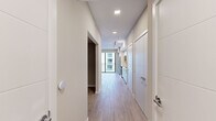 Located in Pompano Beach, Florida, this studio at Mayla 710 presents a thoughtfully designed single-floor layout with a clean, modern aesthetic throughout. Light-toned, wood-look tile flooring runs continuously across the entire space, lending a cohesive and airy feel from entry to living area.

A long, well-lit entry corridor leads into the main living space, lined with recessed and track lighting overhead. The kitchen is positioned along one wall and features crisp white cabinetry extending to the ceiling, a subtle gray tile backsplash, and a full suite of stainless steel appliances including a side-by-side refrigerator with ice and water dispenser, an electric range, built-in microwave, and dishwasher. Ample counter space and generous storage make the kitchen both functional and visually clean.

The open living area is bathed in natural light, drawn in through a full-height sliding glass door that opens to a private balcony with views of the surrounding building exteriors. The sleeping area is a separate, defined space with neutral warm-toned walls and wood-look tile flooring, offering a calm and versatile environment. The overall design is minimal, bright, and well-suited to modern living.