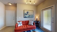 This 1-bedroom, 1-bathroom unit is thoughtfully designed to maximize every square foot of its compact footprint. The open living area serves as the heart of the space, featuring neutral gray walls, concrete-style flooring, and natural light streaming through large windows fitted with blinds and sheer curtains. A ceiling fan overhead adds comfort, while a wall-mounted TV and ample room for seating make it an inviting area to relax or entertain.

The kitchen is a standout feature, boasting dark espresso cabinetry, granite countertops, a white subway tile backsplash, and a full suite of stainless steel appliances including a refrigerator, electric range, and built-in microwave. A peninsula with bar seating provides additional prep space and a casual dining option.

The bedroom is a serene retreat, offering a window that welcomes natural light, neutral tones, and enough space for a full furniture arrangement. The bathroom includes a full soaking tub and shower combo with clean white tile surround, conveniently adjacent to a walk-in closet with built-in shelving and hanging storage. The overall ambiance is modern and functional, with a cohesive design throughout.
