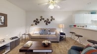 This single-floor residence offers a thoughtfully designed layout that balances comfort and functionality across multiple living spaces. The living room serves as the heart of the home, featuring plush carpeting, a ceiling fan, and generous wall space, creating a warm and inviting atmosphere for relaxation and entertaining. Adjacent to the living area, the dining room benefits from a large window that fills the space with natural light, complemented by a stylish pendant light fixture overhead and soft carpeted flooring underfoot. The kitchen is well-equipped with ample white cabinetry extending to the ceiling, providing generous storage, along with a full-size range and smooth white countertops set against tile flooring — a practical and clean workspace. The residence includes multiple bedrooms, each finished with plush carpet, ceiling fans, and sizable windows that invite natural light. The primary bedroom connects directly to a dedicated en-suite bathroom, which features an extended double vanity with white cabinetry, a large mirror, and tile flooring, offering a functional and organized personal retreat. A second bedroom provides equal comfort with its own ample space and window views. Throughout the residence, a cohesive neutral color palette and consistent finishes create a unified and welcoming ambiance.