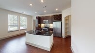 Located at 21201 Emerald Mist Pkwy in Spring, TX, this single-floor residence offers a thoughtfully designed open-concept layout with a blend of refined finishes throughout. The kitchen serves as a central highlight, featuring rich dark cabinetry that extends to the ceiling, stainless steel appliances including a refrigerator, range, and built-in microwave, a dark granite island with an undermount sink, a tile backsplash, recessed lighting, and a distinctive built-in wine rack. An arched entryway with built-in shelving adds architectural character adjacent to the kitchen. The open living area flows seamlessly from the kitchen, showcasing warm hardwood-style flooring and a sliding glass door that invites natural light and outdoor views. The bedrooms are carpeted for comfort and equipped with ceiling fans and multiple windows with blinds that frame greenery outside. The primary bathroom is well-appointed with dark wood cabinetry, dual undermount sinks set in granite countertops, large framed mirrors, hardwood-style flooring, and a glass-enclosed walk-in shower. A spacious walk-in closet with built-in shelving and hanging rods provides ample storage. Throughout the residence, neutral wall tones and natural light create a bright, welcoming ambiance.