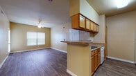 Located at 535 Gembler Rd in San Antonio, Texas, this single-floor unit offers a functional and well-organized layout designed for comfortable everyday living. The entryway opens into a spacious living area featuring rich wood-look flooring, a ceiling fan, and a glass-paned door that invites natural light while providing access to the outdoors. The open-concept design connects the living space seamlessly to the kitchen and dining area. The kitchen is equipped with warm oak cabinetry — both upper and lower — dark laminate countertops, a peninsula breakfast bar with overhead cabinetry, and white appliances including a range, dishwasher, refrigerator, and microwave. A pendant light fixture adds a subtle decorative touch above the dining area. The two bedrooms are carpeted for comfort, each featuring a ceiling fan, blinds-covered windows for natural light and privacy, and ample wall space. The unit includes two full bathrooms, both finished with wood-look tile flooring, tub-shower combinations with tiled surrounds, and oak vanity cabinetry. The primary bathroom features an extended vanity with a large mirror and Hollywood-style lighting. Neutral warm-toned walls throughout the unit create a cohesive and inviting atmosphere.