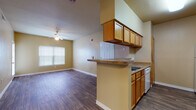 Located at 535 Gembler Rd in San Antonio, Texas, this single-floor unit offers a functional and well-organized layout designed for comfortable everyday living. The entryway opens into a spacious living area featuring rich wood-look flooring, a ceiling fan, and a glass-paned door that invites natural light while providing access to the outdoors. The open-concept design connects the living space seamlessly to the kitchen and dining area. The kitchen is equipped with warm oak cabinetry — both upper and lower — dark laminate countertops, a peninsula breakfast bar with overhead cabinetry, and white appliances including a range, dishwasher, refrigerator, and microwave. A pendant light fixture adds a subtle decorative touch above the dining area. The two bedrooms are carpeted for comfort, each featuring a ceiling fan, blinds-covered windows for natural light and privacy, and ample wall space. The unit includes two full bathrooms, both finished with wood-look tile flooring, tub-shower combinations with tiled surrounds, and oak vanity cabinetry. The primary bathroom features an extended vanity with a large mirror and Hollywood-style lighting. Neutral warm-toned walls throughout the unit create a cohesive and inviting atmosphere.