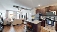 Located at 600 NW Cherrycreek Ln in Ankeny, Iowa, this thoughtfully designed one-bedroom, one-bathroom residence makes excellent use of its compact footprint across a single floor. The open-concept layout connects the kitchen and living areas seamlessly, creating a functional and welcoming atmosphere throughout.

The kitchen is a standout feature, showcasing rich dark-toned cabinetry that reaches toward the ceiling, light quartz countertops, and a full suite of stainless steel appliances including a refrigerator, range, microwave, and dishwasher. A center island with seating provides additional prep space and a casual dining option, while open shelving adds a modern touch.

The living room is bright and airy, benefiting from natural light streaming through large windows and a glass-paneled entry door. Warm hardwood-style flooring runs throughout, and a ceiling fan adds comfort year-round.

The bedroom is a comfortable and serene retreat, featuring large windows that invite natural light and offer outdoor views, along with a ceiling fan and room for ample furnishings. The bathroom connects conveniently to an in-unit laundry area equipped with a stacked washer and dryer, adding a practical and desirable amenity to this well-rounded residence.