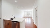 This Sullivan Place one-bedroom apartment, model A1D 5-1150, offers a compact yet well-designed living space of 610 square feet. The open-concept layout maximizes the use of space, seamlessly blending the living room and kitchen areas. The kitchen boasts modern wood-tone cabinetry, stainless steel appliances, and a sleek white countertop with a convenient breakfast bar.

The primary bedroom, measuring 140 square feet, features plush carpeting and a large window that floods the space with natural light. An adjoining walk-in closet provides ample storage. The bathroom is elegantly appointed with a wooden vanity, marble-look flooring, and a combination tub-shower.

Throughout the apartment, warm-toned hardwood flooring adds a touch of sophistication, while crisp white walls create a bright, airy atmosphere. The living area's large windows offer picturesque views of the surrounding area. With its thoughtful design and modern amenities, this apartment efficiently utilizes every square foot to create a comfortable and stylish living space.