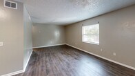 Located at 2401 Jammes Rd in Jacksonville, FL, this single-floor, one-bedroom, one-bathroom unit offers a practical and well-organized layout. Dark hardwood-style flooring flows consistently throughout the living room, hallway, and bedroom, providing a cohesive and clean aesthetic. The living room is a generously sized open area featuring neutral warm-gray walls, a textured popcorn ceiling, and multiple windows that allow natural light to fill the space. A full wall of mirror panels along one side of the hallway visually expands the interior, enhancing the sense of openness as you move through the unit. The kitchen is outfitted with ample white cabinetry above and below, complemented by a striking marble-pattern countertop that adds a refined touch. The bedroom features neutral gray walls, hardwood-style flooring, and a closet, creating a quiet and comfortable retreat. The bathroom includes a full-size tub and shower combination with white tile surround, maintaining the unit's clean, bright finishes. Throughout the space, white baseboards and trim provide crisp contrast against the neutral walls, contributing to a tidy, well-maintained appearance overall.