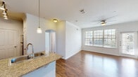 Located at 10700 Lakeline Mall Dr in Austin, TX, this one-bedroom, one-bathroom residence offers a well-designed layout with thoughtful finishes throughout. The open-concept kitchen and living area serves as the heart of the home, featuring rich hardwood-style flooring, crown molding, and a ceiling fan that enhances airflow and comfort. The kitchen is outfitted with dark espresso cabinetry, granite countertops, stainless steel appliances including an electric range and microwave, a tile backsplash, and elegant pendant lighting over the double-basin sink. The living area receives abundant natural light through large windows and includes access to an exterior door. The spacious bedroom continues the hardwood-style flooring and crown molding, with a large window allowing ample daylight and a ceiling fan overhead. It connects directly to a generously sized walk-in closet featuring dual clothing rods and built-in shelving. The full bathroom is finished with dark cabinetry, granite countertops, wood-look flooring, and a tiled soaking tub and shower combination. A dedicated laundry area with a top-loading washer and overhead shelving adds everyday convenience. Carpeted staircases provide access between levels of the building.