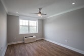 Located at 7 Continental Pl in Glen Cove, NY, this single-floor unit showcases a thoughtfully designed layout with modern finishes throughout. The kitchen is a standout feature, equipped with stainless steel appliances including a French door refrigerator, gas range with over-the-range microwave, and dishwasher. White shaker-style cabinetry with glass-front uppers pairs with a marble-look quartz backsplash and countertops, while a peninsula with pendant lighting provides additional workspace and visual separation from the living area. Warm-toned hardwood flooring flows seamlessly throughout the entire unit, creating a cohesive and inviting atmosphere. Crown molding adds a refined architectural detail to the living spaces, which benefit from recessed lighting and a ceiling fan. Bedrooms are generously proportioned, each featuring large windows that bring in natural light and views of surrounding greenery, along with individual wall units for climate control. The bathroom is well-appointed with a combination tub and shower enclosed by a glass panel, white subway tile surround, and a vanity topped with marble-look counters. The open living and dining area connects directly to the kitchen, supporting a practical and modern flow throughout the space.
