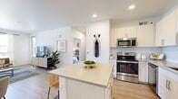 This single-story residence offers a thoughtfully arranged floor plan that maximizes functionality and comfort. The open-concept kitchen and living area serves as the heart of the home, featuring light wood-style flooring that runs throughout the space. The kitchen is outfitted with white shaker-style cabinetry, a classic subway tile backsplash, stainless steel appliances including a range, microwave, dishwasher, and refrigerator, and a center island with a light quartz countertop and seating for two—ideal for casual dining or meal prep.

The adjacent living room receives ample natural light through large windows that offer views of the surrounding neighborhood. The bright, neutral color palette and recessed lighting contribute to an open, airy ambiance throughout the common areas.

The bedroom is a well-proportioned retreat featuring a ceiling fan, a large window with outdoor views, and direct access to a dedicated closet with built-in storage. The bathroom is finished with light cabinetry, a single-sink vanity, a large mirror, and the same wood-style flooring found throughout the unit, creating a cohesive and clean aesthetic from room to room.