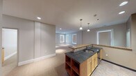 Located on Main Street in Buffalo, NY, this single-floor unit offers a thoughtfully designed open layout with a neutral color palette and consistent finishes throughout. The kitchen serves as the focal point of the main living area, featuring light maple cabinetry, dual countertop surfaces—a granite-topped island with an integrated sink and open shelving below, and a separate peninsula with warm-toned granite—alongside stainless steel appliances including a gas range, built-in microwave, and French door refrigerator. Pendant lighting and recessed fixtures illuminate the space effectively. The open-plan living and dining area extends from the kitchen, carpeted throughout and lined with multiple windows fitted with roller shades, allowing ample natural light. A dedicated laundry closet with a stacked washer and dryer unit is conveniently accessible from the main living space. Private rooms include carpeted bedrooms, one featuring a sliding wood-door closet with built-in shelving. The bathroom includes a spacious walk-in glass-enclosed shower with a built-in bench seat, tile surround, and dual shower fixtures. Clean white trim and soft gray walls contribute to a cohesive, modern aesthetic throughout.