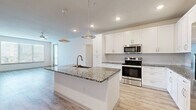 Located in Tampa, FL, this single-story, 3-bedroom, 2-bathroom home offers a bright and modern living experience with clean finishes throughout. The open-concept kitchen and living area serves as the heart of the home, featuring a large granite-topped island with a built-in sink, sleek white cabinetry, stainless steel appliances including a range, microwave, and refrigerator, and stylish pendant lighting overhead. Light wood-look flooring flows throughout the main living areas, enhancing the airy, contemporary feel. Large windows allow abundant natural light to fill the living space, which also provides access to a private patio. The three bedrooms are well-proportioned, with the primary bedroom offering generous dimensions, plush carpeting, a ceiling fan, and a dedicated en-suite bathroom. The primary bath features granite countertops, white cabinetry, a walk-in shower, and large-format tile flooring. The secondary bathroom mirrors the same refined aesthetic with a granite vanity, white cabinetry, and a tiled tub-shower combination. Each bedroom benefits from dedicated closet space, with the home offering six closets in total, providing exceptional storage. A connecting hallway ties the layout together seamlessly, making this home as functional as it is visually appealing.