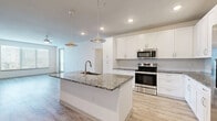 Located in Tampa, FL, this single-story, 3-bedroom, 2-bathroom home offers a bright and modern living experience with clean finishes throughout. The open-concept kitchen and living area serves as the heart of the home, featuring a large granite-topped island with a built-in sink, sleek white cabinetry, stainless steel appliances including a range, microwave, and refrigerator, and stylish pendant lighting overhead. Light wood-look flooring flows throughout the main living areas, enhancing the airy, contemporary feel. Large windows allow abundant natural light to fill the living space, which also provides access to a private patio. The three bedrooms are well-proportioned, with the primary bedroom offering generous dimensions, plush carpeting, a ceiling fan, and a dedicated en-suite bathroom. The primary bath features granite countertops, white cabinetry, a walk-in shower, and large-format tile flooring. The secondary bathroom mirrors the same refined aesthetic with a granite vanity, white cabinetry, and a tiled tub-shower combination. Each bedroom benefits from dedicated closet space, with the home offering six closets in total, providing exceptional storage. A connecting hallway ties the layout together seamlessly, making this home as functional as it is visually appealing.