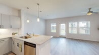 Located in Porter, TX, this thoughtfully designed single-story home offers a clean, modern aesthetic throughout. Light wood-tone flooring flows seamlessly across the entire layout, complementing the crisp white walls and creating a bright, cohesive atmosphere.

The open-concept living room is generously sized, bathed in natural light from multiple windows and a glass door that opens to outdoor views. A ceiling fan with a contemporary gold-toned fixture adds both comfort and style to the airy space.

The kitchen is a standout feature, outfitted with gray shaker-style cabinetry, granite countertops, a classic white subway tile backsplash, and a full suite of stainless steel appliances including a French door refrigerator, gas range, and built-in microwave. A peninsula with an integrated sink and pendant lighting provides additional workspace and casual dining potential.

The bedroom is a comfortable, well-lit retreat with a large window, ceiling fan, and direct access to a dedicated closet featuring a full-width hanging rod system. The bathroom is clean and functional, offering a tiled tub-shower combo, and conveniently shares space with an in-unit washer and dryer area. This home balances practicality and modern style in a compact, efficient footprint.