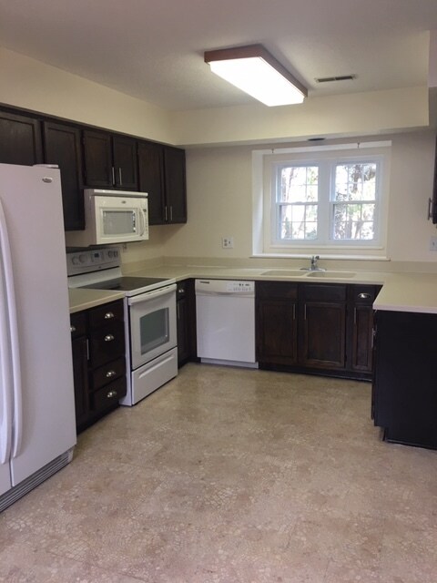 Lovely kitchen with dark wood cabinetry, corian countertop, Whirlpool white appliances, and new cabinet hardware. - 9660 Windjammer