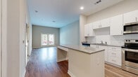 Located at 7326 Wallace Rd in Charlotte, NC, this well-appointed single-floor residence offers a thoughtfully designed open-concept layout. The kitchen serves as a central highlight, featuring crisp white cabinetry, granite countertops, a subway tile backsplash, and a full suite of stainless steel appliances including a range, microwave, dishwasher, and refrigerator. A peninsula island provides additional counter space and a natural divide between the kitchen and the adjoining living area. The living space is bright and welcoming, with warm hardwood-style flooring that extends throughout and a set of French doors that invite natural light and offer views of the outdoors. The bedroom is a comfortable, well-lit room with a large window overlooking greenery, continuing the hardwood-style flooring for a cohesive feel. The bathroom is cleanly finished with a white vanity, granite countertop, large mirror, and light wood-tone flooring. Recessed lighting, neutral wall tones, and modern hardware contribute to a clean, contemporary aesthetic throughout. A louvered closet door adds a practical storage solution near the entry. Overall, this space presents a modern, move-in-ready interior with consistent, quality finishes from room to room.