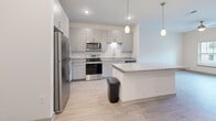 This single-story residence in Mount Juliet, Tennessee offers a thoughtfully designed layout with a clean, contemporary aesthetic throughout. The kitchen serves as a standout feature, outfitted with granite countertops, crisp white subway tile backsplash, gray cabinetry, and a full suite of stainless steel appliances including a refrigerator, range, microwave, and dishwasher. A kitchen island with pendant lighting above provides additional counter space and a natural gathering point that connects seamlessly to the adjoining living area.

The living room is bright and welcoming, finished with light wood-style flooring and a ceiling fan. A door with an adjacent window opens to the outdoors, allowing natural light to fill the space and providing direct exterior access. The bedroom features neutral carpet, a ceiling fan, and a window with outdoor views, contributing to a calm, restful atmosphere. A closet with wire shelving provides practical storage.

The bathroom is finished with wood-look tile flooring, a granite-top vanity with gray cabinetry, a large mirror, and accessibility grab bars, reflecting both style and functionality. Throughout the unit, neutral tones and consistent finishes create a cohesive, modern living environment.