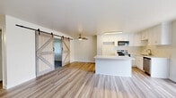Located at 6401 Warner Ave in Huntington Beach, CA, this 2-bedroom, 2-bathroom residence offers a well-designed single-floor layout that maximizes comfort and functionality. The open-concept living and kitchen area serves as the heart of the home, featuring light wood-style flooring that flows throughout. A standout pair of sliding barn doors adds a charming farmhouse touch, seamlessly connecting the living space to the rest of the home. The kitchen is equipped with white shaker-style cabinetry, stainless steel appliances including an electric range and dishwasher, a built-in microwave, and a peninsula island that provides additional prep and dining space. A ceiling fan overhead enhances air circulation in the combined living area. Natural light enters through vertical blind-covered windows and a sliding glass door in the primary bedroom, which offers generous proportions and hardwood-style flooring. The second bedroom features plush carpeting and a window with vertical blinds. Both bedrooms include wall heater units. The hallway connects the bedrooms to the two bathrooms with clean, neutral finishes throughout. The overall ambiance is bright, clean, and move-in ready, reflecting a modern yet approachable aesthetic.