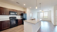 This well-appointed 2-bedroom, 2-bathroom residence in Austin, TX offers a thoughtfully designed single-floor layout that balances comfort and functionality. The open-concept kitchen and living area serves as the heart of the home, featuring a large central island with granite countertops, an undermount sink, and elegant pendant lighting overhead. Rich dark-wood cabinetry pairs with black appliances, including a range, microwave, and refrigerator, while wood-style flooring extends seamlessly into the living area, which is topped with a ceiling fan and brightened by large windows with outdoor views. The bedrooms offer a calm retreat, with plush carpeting, crisp white walls, and generous natural light from well-positioned windows fitted with blinds. The primary bedroom is a comfortable size and connects to a dedicated bathroom and a walk-in closet outfitted with wire shelving for ample storage. A second closet serves the additional bedroom. Both bathrooms are finished with light wood-style flooring and clean, neutral tones. A laundry area with hookups is also included. Recessed lighting and a neutral color palette throughout lend the space a bright, modern ambiance suited for everyday living in Austin.