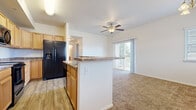 This single-floor residence offers a functional and comfortable layout designed for everyday living. The kitchen is equipped with light wood cabinetry, stone-toned countertops, wood-look vinyl flooring, and black appliances including a side-by-side refrigerator with ice and water dispenser, a range, and a dishwasher. A peninsula with a breakfast bar connects the kitchen to the living area, creating an open, cohesive space ideal for entertaining. The living room features plush carpeting, a ceiling fan, and a sliding glass door that opens onto a private balcony with outdoor views, allowing natural light to fill the space. A dedicated dining area sits adjacent to the living room, accented by a chandelier and additional windows fitted with white horizontal blinds. The bedrooms are carpeted and well-sized, each offering natural light through windows with blinds and generous closet space, including sliding-door closets in multiple rooms. The bathroom features a full soaking tub and shower combination with built-in shelving and tile flooring. A separate laundry room includes washer and dryer hookups, a dryer vent, and tile flooring, providing added convenience. Throughout the residence, a neutral color palette and consistent finishes create a clean, cohesive ambiance.