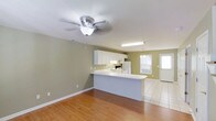 This two-bedroom, two-bathroom townhouse is thoughtfully laid out across two floors, offering a practical and comfortable living environment. The main level showcases an open-concept design that seamlessly connects the living area and kitchen, creating a bright and functional shared space. The kitchen features white cabinetry, a peninsula-style breakfast bar with a light countertop, and includes a full suite of appliances. A ceiling fan overhead provides year-round comfort to the living area, which is finished with warm hardwood flooring. The kitchen and adjoining dining area transition to tile flooring, adding durability and easy maintenance where it matters most. Natural light filters through multiple windows, lending a welcoming atmosphere to the main living space. A pendant light fixture adds a subtle decorative touch above the dining area. The light green walls throughout the main floor create a calm, neutral backdrop that complements the clean white trim and cabinetry. With two full bathrooms and two bedrooms distributed across its two floors, this townhouse provides ample space and privacy, making it well-suited for a variety of living arrangements.
