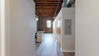 Located at 1601 Walnut St in Kansas City's vibrant Crossroads Arts District, this loft-style unit blends industrial character with modern finishes across a single, efficiently designed floor. The space immediately impresses with its soaring exposed wood beam and rafter ceilings, visible ductwork, and original structural columns — hallmarks of a thoughtfully converted historic building. Light hardwood-style flooring runs throughout, complementing the bright, neutral palette of the walls.

The kitchen is a standout feature, offering a peninsula with granite-style countertops, light wood cabinetry, stainless steel appliances including a refrigerator and dishwasher, and pendant lighting overhead. Track lighting adds a contemporary touch to the open layout. The living area benefits from the dramatic ceiling height, creating an airy, open ambiance despite the unit's compact footprint.

The bathroom is clean and functional, with hardwood-style flooring continuing from the main living space. Exposed brick visible through the bathroom doorway reinforces the industrial aesthetic. A dedicated laundry room provides the convenience of a full-size washer and dryer. Additional practicality is offered through a closet, hallway, and entrance area, ensuring smart use of every square foot in this well-appointed urban retreat.