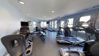 Located at 800 Runaway Bay Ln in Mount Pleasant, South Carolina, this fitness center offers a well-equipped, single-floor workout facility designed to support a comprehensive exercise routine. The space features light teal-painted walls, recessed ceiling lighting, and multiple windows that invite natural light and views of the surrounding greenery, creating a bright and energizing atmosphere throughout.

The cardio section is generously stocked with treadmills, elliptical trainers, and a stair climber, providing a variety of options for cardiovascular workouts. A Matrix cable machine and multi-function weight station anchor the strength training area, complemented by a dedicated free weights zone featuring a full rack of dumbbells and an adjustable bench. A rowing machine adds further versatility to the equipment lineup.

Wall-mounted flat-screen televisions are positioned throughout the room, allowing users to stay entertained during their workouts. A large mirror along one wall enhances the sense of space and provides visual feedback for form and technique. The dark rubberized flooring offers both durability and safety underfoot. Informational postings and a hand sanitizer station reflect attention to cleanliness and user convenience. Overall, the facility presents a clean, functional, and well-maintained environment suitable for a wide range of fitness needs.