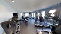 Located at 800 Runaway Bay Ln in Mount Pleasant, South Carolina, this fitness center offers a well-equipped, single-floor workout facility designed to support a comprehensive exercise routine. The space features light teal-painted walls, recessed ceiling lighting, and multiple windows that invite natural light and views of the surrounding greenery, creating a bright and energizing atmosphere throughout.

The cardio section is generously stocked with treadmills, elliptical trainers, and a stair climber, providing a variety of options for cardiovascular workouts. A Matrix cable machine and multi-function weight station anchor the strength training area, complemented by a dedicated free weights zone featuring a full rack of dumbbells and an adjustable bench. A rowing machine adds further versatility to the equipment lineup.

Wall-mounted flat-screen televisions are positioned throughout the room, allowing users to stay entertained during their workouts. A large mirror along one wall enhances the sense of space and provides visual feedback for form and technique. The dark rubberized flooring offers both durability and safety underfoot. Informational postings and a hand sanitizer station reflect attention to cleanliness and user convenience. Overall, the facility presents a clean, functional, and well-maintained environment suitable for a wide range of fitness needs.