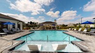 Located at 4215 Midvale Dr in Wilmington, NC, this single-level outdoor amenity space offers a well-appointed community retreat designed for relaxation and social gatherings. At its centerpiece is a generously sized resort-style swimming pool with crystal-clear water, entry steps, and in-water lounge chairs, all set against a backdrop of open sky and lush greenery. The pool deck is finished with attractive paver stonework and lined with chaise lounges and bold blue market umbrellas, providing ample space for sunbathing and leisure.

Adjacent to the pool is a spacious covered pavilion featuring a warm wood-paneled ceiling supported by crisp white columns. This sheltered gathering space is outfitted with comfortable wicker and upholstered seating, dining tables with chairs, and a built-in outdoor fireplace clad in white brick, creating a welcoming atmosphere in any season. A wall-mounted television adds entertainment convenience, while views of the pool and surrounding neighborhood greenery enhance the open, airy feel. Outdoor grills are also available nearby, making the area ideal for community cookouts and events. The overall design blends coastal charm with modern amenities, delivering a polished and inviting outdoor experience.