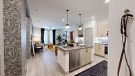 Located at 7777 Manderville Ln in Dallas, TX, this well-designed 2-bedroom, 2-bathroom residence offers a cohesive modern aesthetic across a single floor. The open-concept kitchen and living area serves as the heart of the home, featuring light wood cabinetry, stainless steel appliances, a center island with pendant lighting overhead, and light wood-style flooring that flows seamlessly throughout. The living room is anchored by a striking textured accent wall and large windows that invite abundant natural light, with direct access to an outdoor area. Both bedrooms are carpeted and generously sized, each offering windows with blinds and drapes. The primary bedroom is a comfortable retreat, while the second bedroom features a bold navy blue accent wall and ceiling fan. Each bathroom is well-appointed, with the primary bath offering a dual-sink vanity with wood cabinetry, grey countertops, marble-style tile flooring, and a combination tub and separate glass shower. Two dedicated closets provide ample storage, with wire shelving systems for organization. A connecting hallway ties the layout together efficiently, rounding out a residence that balances contemporary style with practical everyday functionality.