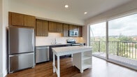 This single-floor unit offers a thoughtfully designed layout that balances functionality with contemporary style. The kitchen serves as the centerpiece of the space, showcasing rich dark-stained cabinetry that reaches toward the ceiling, providing ample storage. A white quartz countertop island anchors the kitchen and offers additional prep and seating space. The backsplash features classic white subway tile, while a full suite of stainless steel appliances — including a refrigerator, dishwasher, electric range, and over-the-range microwave — completes the space. Warm wood-tone luxury vinyl plank flooring runs throughout the unit, creating a cohesive and easy-to-maintain aesthetic. Adjacent to the kitchen, a large sliding glass door opens onto a private balcony, allowing natural light to fill the interior and offering open views of the surrounding treetops and cityscape. A dedicated in-unit laundry closet houses a stacked washer and dryer for added convenience. The bedroom is a clean, bright room with neutral walls and continued wood-tone flooring, offering a versatile and comfortable retreat. The full bathroom features a tub/shower combination, a dark-toned vanity with white countertop, and matching flooring, maintaining the unit's cohesive modern design throughout.