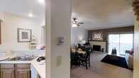 This two-floor residence offers a thoughtfully designed layout that balances comfort and functionality. The main living area is anchored by a classic fireplace framed by a clean white mantel, creating a warm and inviting focal point. A ceiling fan overhead ensures year-round comfort while adding to the room's approachable charm. The living space flows seamlessly into a dedicated dining area, accommodating a full dining set ideal for everyday meals and entertaining alike. Neutral-toned carpeting throughout the living and dining spaces contributes to a soft, cohesive aesthetic. Adjacent to the dining area, the kitchen features light countertops and ample workspace, with an open pass-through that maintains a sense of connectivity between the cooking and living zones. The textured ceiling and neutral wall tones throughout provide a versatile backdrop suited to a variety of interior styles. With two floors of living space, this residence provides room for distinct living and private areas, making it a practical and comfortable home. The overall ambiance is welcoming and well-appointed, with functional details integrated throughout.