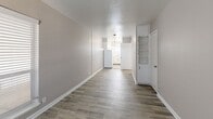 Located at 212 S Cooper St in Arlington, TX, this single-story, one-bedroom, one-bathroom unit offers a well-organized layout designed to maximize every square foot. The combined living, dining, and kitchen area forms the heart of the home, featuring wood-look plank flooring in a warm gray tone that flows throughout the space. Neutral taupe walls and crisp white trim create a clean, cohesive aesthetic, while multiple windows with horizontal blinds allow natural light to fill the rooms.

The living area provides a welcoming entrance through a paneled front door flanked by windows, lending an open and airy feel. A built-in shelving unit adds a functional decorative touch to the main living space. The kitchen is positioned at the rear, featuring white cabinetry, a full-size refrigerator, and a pendant light overhead.

The bedroom is a comfortable, well-proportioned retreat equipped with a ceiling fan and light fixture, a window for natural light, and direct access to a dedicated walk-in closet with built-in shelving. Additional storage is provided by two more closets throughout the unit.

The bathroom showcases updated finishes including a marble-style vanity countertop, white shaker-style cabinetry with black hardware, a tub-shower combination, tile-look flooring, and a window for ventilation. The overall design is clean, modern, and move-in ready.
