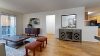 Located at 3150 S Tamarac Dr in Denver, Colorado, this one-bedroom, two-bathroom residence offers a thoughtfully arranged single-floor layout. Warm hardwood flooring flows throughout the main living areas, beginning at a dedicated dining space illuminated by a pendant light fixture and accented by mirrored closet doors that add depth to the room. The open sightline connects the dining area seamlessly to the living room, which features a neutral color palette, a large wall-mounted art piece, a sliding glass door providing natural light, and access to a private balcony. The kitchen is equipped with oak cabinetry extending to the ceiling, dark granite-style countertops, a double sink, a dishwasher, and black appliances, all set on durable tile flooring. The spacious bedroom is carpeted for comfort and includes a window with vertical blinds, generous closet access, and a baseboard heating system. Two full bathrooms serve the unit, each featuring oak vanity cabinetry with dark countertops and large mirrors; one includes a full tub-shower combination with white tile surround. Three closets throughout the unit ensure abundant storage. The textured ceilings are consistent throughout, contributing to the cohesive and functional design of this well-appointed Denver residence.