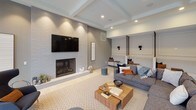This single-floor communal space is designed with a contemporary aesthetic, combining open-plan living with distinct functional zones. The lounge area serves as the heart of the space, anchored by a floor-to-ceiling tiled fireplace with a wall-mounted television above, flanked by built-in bench seating with individual sconce lighting and accent pillows. A generous sectional sofa and layered area rugs create an inviting, relaxed atmosphere beneath coffered ceilings with recessed lighting.

Adjacent to the lounge, a sleek wet bar features a dark perforated metal island with bar stool seating, subway-tiled backsplash, under-counter appliances, and a sink — well-suited for entertaining. The game room area includes a full-size pool table, adding a recreational element to the overall layout.

Floor-to-ceiling sliding glass doors flood the space with natural light and connect seamlessly to an outdoor terrace equipped with bar-height communal seating and overhead pergola structures. Light wood-tone flooring runs throughout, complementing the neutral gray palette and industrial-modern design details that define the space's overall character.