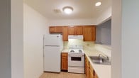 This single-floor unit at 126 offers a practical and well-organized layout designed for comfortable everyday living. The kitchen is efficiently arranged with warm honey-toned wood cabinetry, light countertops, a stainless steel sink, and white appliances including a refrigerator, electric range, and overhead ventilation hood. Tile flooring in the kitchen provides easy maintenance, while a pass-through opening connects the kitchen to the living area, creating an open and communicative flow between spaces. The living and dining areas feature plush carpeting throughout, neutral walls, and recessed lighting that contributes to a bright, welcoming atmosphere. A half-wall with a support column adds architectural definition between the kitchen and main living space. The bedrooms are generously sized, each outfitted with soft carpeting and windows fitted with blinds that allow for natural light and privacy. The bathroom includes a full tub and shower combination with white tile surround, complemented by tile flooring and clean, straightforward fixtures. Overall, the unit presents a neutral, move-in-ready palette with functional design choices suited for a range of occupants.