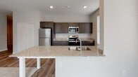 This single-story residence presents a cohesive, contemporary design throughout its well-organized floor plan. The kitchen serves as a central highlight, featuring dark espresso-toned cabinetry, granite countertops, and a full suite of stainless steel appliances including a refrigerator, range, microwave, and dishwasher. A peninsula with an undermount sink and additional granite surface extends into the adjacent living and dining area, creating an open, connected feel. Wood-look flooring runs through the kitchen and main living areas, while large windows fitted with blinds allow controlled natural light into the space.

The living area offers a comfortable, open layout with neutral carpet and direct sightlines to the kitchen. Bedrooms continue the neutral palette with plush carpet, multiple windows for natural light, and clean white walls. The primary bathroom features tile flooring, dark cabinetry with granite countertops, an undermount sink, and direct access to a spacious walk-in closet with wire shelving. A secondary bathroom mirrors the design aesthetic with consistent dark cabinetry, granite countertops, and tile flooring. Throughout the residence, consistent finishes and neutral tones create a clean, move-in-ready environment.