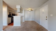 This single-floor residence offers a practical and efficient layout across a comfortable footprint, featuring one bedroom, one bathroom, a combined kitchen and living area, and a dedicated closet. The living room serves as the focal point of the home, highlighted by a tiled fireplace and sliding glass door that opens to an outdoor balcony, allowing natural light to fill the carpeted space. A textured ceiling and neutral gray walls contribute to a clean, understated aesthetic throughout. The kitchen is positioned adjacent to the living area and is separated by a peninsula counter, providing both workspace and a casual bar-style divide. The kitchen features hardwood-style flooring, black appliances including an electric range and refrigerator, a double sink, and ample cabinet storage with under-counter space. The bedroom offers a generous, carpeted space with a ceiling fan, a sliding glass door to an additional outdoor area, and easy access to a dedicated walk-in closet equipped with built-in shelving and hanging rods. The bathroom is clean and functional, featuring a tiled tub-shower combination, a single vanity with a speckled countertop, and hardwood-style flooring. Ceiling fans are present in both the living and bedroom areas, enhancing year-round comfort throughout the home.