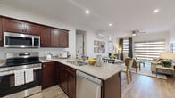 This thoughtfully designed single-story residence offers two bedrooms, three bathrooms, and a functional layout that makes excellent use of its space. The open-concept kitchen is a standout feature, showcasing rich dark cabinetry, granite countertops, stainless steel appliances including a refrigerator and dishwasher, and a peninsula island with bar seating — ideal for casual dining or entertaining. The kitchen flows seamlessly into the dining and living areas, where large windows dressed with layered zebra blinds and drape panels fill the space with natural light. Crown molding and ceiling fans are present throughout, adding classic architectural detail. Each bedroom is comfortably sized and features soft carpeting, ceiling fans, and window treatments. The primary bedroom includes direct access to an en-suite bathroom and a dedicated closet with built-in wire shelving. A second bedroom also benefits from easy bathroom access and its own closet. The bathrooms are finished with dark wood vanities and granite countertops, complementing the overall design palette. Wood-look plank flooring runs through the main living areas and hallways, providing a warm and cohesive aesthetic. Mini-split HVAC units are present in multiple rooms, offering individualized climate control throughout the residence.