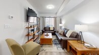 Located at 30 George St S in Cambridge, Ontario, this well-appointed one-bedroom, one-bathroom unit offers a thoughtfully organized layout across a single floor. Light-toned hardwood flooring runs throughout the space, lending warmth and visual continuity to each room.

The living room serves as the heart of the unit, comfortably accommodating a full seating arrangement with a wall-mounted television, open shelving, and a coffee table. A window provides natural light and an outward view, while a tray ceiling adds a touch of architectural definition to the room.

The bedroom is generously sized, featuring a tray ceiling, natural light from a window with outdoor views, and ample room for a king-sized bed and additional furnishings such as a dresser and desk. The neutral color palette and light flooring create a calm, restful atmosphere.

The bathroom is clean and modern in design, finished with a stone-topped vanity, white cabinetry with contemporary hardware, and light hardwood flooring. Crisp white panel doors and bright finishes contribute to the overall fresh and airy feel of the space.

A utility room completes the layout, providing practical storage and functional support. Throughout the unit, the design emphasizes clean lines, neutral tones, and efficient use of space, making it a comfortable and practical residence in Cambridge's urban core.
