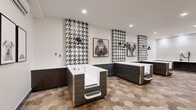 Located at 5905 Caravan Ct in Orlando, FL, this purpose-built pet grooming facility combines functional design with striking aesthetic choices. The space is composed of a main grooming room and a connecting hallway, together offering a generous and well-organized layout.

The grooming room is the centerpiece of the facility, housing multiple freestanding dog bathing tubs finished in a dark wood-grain exterior with built-in entry steps for easy pet access. Each tub station is framed by bold vertical columns of black-and-white houndstooth tile, creating dramatic visual anchors against the crisp white walls. Black industrial-style wall sconces provide focused lighting at each station, contributing to the space's modern yet boutique ambiance.

The floors throughout are clad in warm-toned hexagonal ceramic tiles that add texture and visual interest while remaining practical and easy to maintain. A dedicated grooming area features a wall-mounted vacuum/dryer system and a built-in white countertop with dark tile wainscoting. The hallway entry area includes a wall-mounted split air conditioning unit, circular leash hooks, and framed black-and-white dog portrait artwork, reinforcing the pet-centric theme. Recessed ceiling lighting illuminates the entire space evenly, creating a clean, welcoming environment for both pets and their owners.