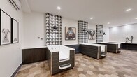 Located at 5905 Caravan Ct in Orlando, FL, this purpose-built pet grooming facility combines functional design with striking aesthetic choices. The space is composed of a main grooming room and a connecting hallway, together offering a generous and well-organized layout.

The grooming room is the centerpiece of the facility, housing multiple freestanding dog bathing tubs finished in a dark wood-grain exterior with built-in entry steps for easy pet access. Each tub station is framed by bold vertical columns of black-and-white houndstooth tile, creating dramatic visual anchors against the crisp white walls. Black industrial-style wall sconces provide focused lighting at each station, contributing to the space's modern yet boutique ambiance.

The floors throughout are clad in warm-toned hexagonal ceramic tiles that add texture and visual interest while remaining practical and easy to maintain. A dedicated grooming area features a wall-mounted vacuum/dryer system and a built-in white countertop with dark tile wainscoting. The hallway entry area includes a wall-mounted split air conditioning unit, circular leash hooks, and framed black-and-white dog portrait artwork, reinforcing the pet-centric theme. Recessed ceiling lighting illuminates the entire space evenly, creating a clean, welcoming environment for both pets and their owners.