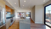 This contemporary single-floor residence showcases a thoughtfully designed open-concept layout that seamlessly connects the kitchen, dining, and living areas. The kitchen is a standout feature, centered around a large granite-topped island with an integrated sink and high-arc faucet. Cabinetry combines rich warm-toned wood uppers with sleek grey lower units, complemented by a subway tile backsplash and stainless steel appliances including a gas range and refrigerator. Recessed lighting and a distinctive coffered ceiling detail above the kitchen add architectural depth.

Wide-plank hardwood flooring flows throughout the space, unifying each area with warmth and continuity. The living area is bright and expansive, benefiting from floor-to-ceiling black-framed windows and sliding glass doors that open to a private balcony, inviting generous natural light and outdoor views of the surrounding neighborhood.

The bedrooms are well-proportioned with neutral tones and continued hardwood flooring. The bathrooms reflect a refined modern aesthetic — one features a wall-mounted trough sink with a dark wood vanity, while another offers a frameless glass walk-in shower with textured tile surround and mosaic pebble flooring. Every detail of this residence reflects clean, contemporary design with quality finishes throughout.