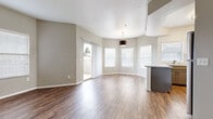This single-floor residence offers a thoughtfully designed open-concept layout that seamlessly connects the living, dining, and kitchen areas. The main living space features rich wood-style flooring and vaulted ceilings that lend a sense of openness and volume. Multiple windows dressed with blinds flood the interior with natural light, while a sliding glass door leads directly to a private covered balcony with views of the surrounding neighborhood greenery.

The kitchen is well-equipped with gray shaker-style cabinetry, light quartz countertops, a classic white subway tile backsplash, and a full suite of stainless steel appliances including a refrigerator, range, microwave, and dishwasher. A breakfast bar peninsula provides additional counter space and casual seating, connecting the kitchen to the living area.

The bedrooms feature plush wall-to-wall carpeting, ceiling fans, and ample natural light from large windows. The bathroom is finished with an extended quartz vanity countertop, gray cabinetry, a large framed mirror, and wood-style flooring, creating a clean and modern aesthetic throughout. Neutral gray-toned walls tie the entire residence together for a cohesive and contemporary feel.