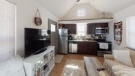 This two-floor residence offers a thoughtfully designed layout with a variety of functional and comfortable living spaces. The heart of the home is an open living and kitchen area distinguished by soaring vaulted ceilings that lend an airy, expansive feel. The kitchen is well-appointed with dark wood cabinetry, granite countertops, stainless steel appliances including a refrigerator, range, microwave, and dishwasher, and wood-look flooring that flows seamlessly into the living area. Natural light filters in through multiple windows fitted with blinds, brightening the main living space. The bedrooms are carpeted for comfort and each includes a ceiling fan with light fixture, providing efficient climate control. One bedroom features an en-suite bathroom corridor complete with a vanity, open closet with hanging storage, and wall-mounted wire organizers, leading directly into a private bathroom with a walk-in shower. A secondary full bathroom includes a walk-in shower stall with a curtain, toilet, and additional shelving for storage. The overall aesthetic is neutral and clean, with white and warm beige tones throughout, creating a welcoming and move-in-ready environment across both floors.